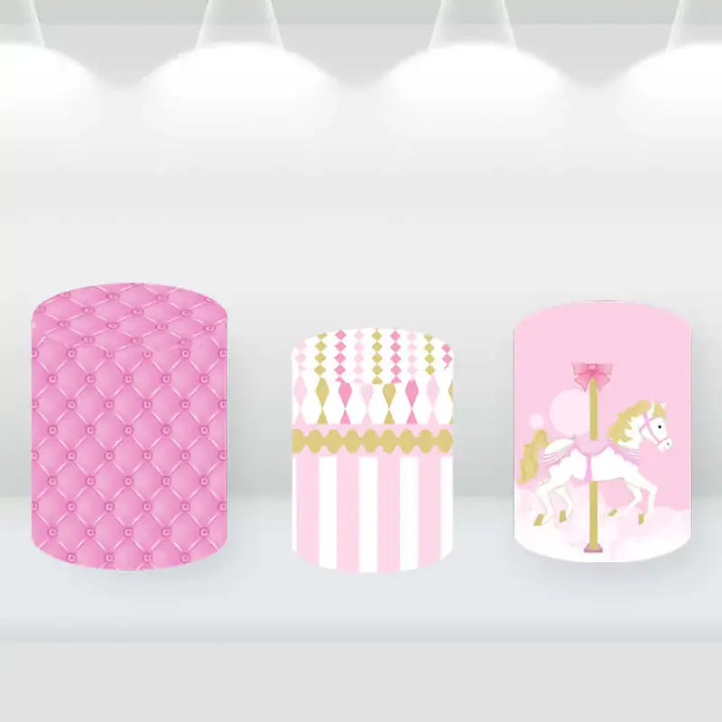 Set of three cylindrical pedestal covers with pink and gold designs, including a carousel horse, quilted pattern, and striped pattern.