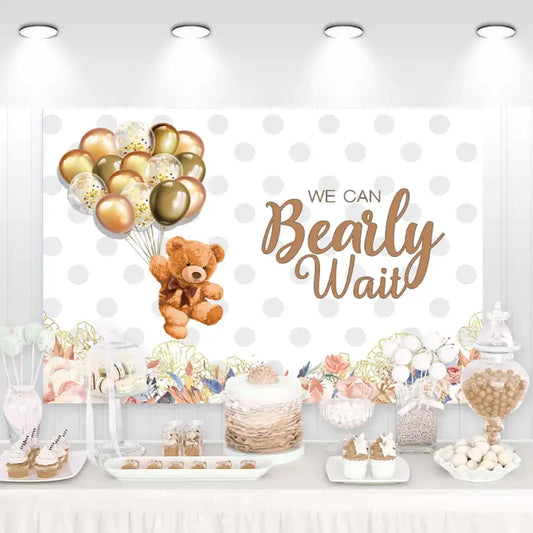 Neutral baby shower backdrop with brown teddy bear, gold and bronze balloons, polka dot background, and floral accents – 'We Can Bearly Wait' theme for elegant celebrations