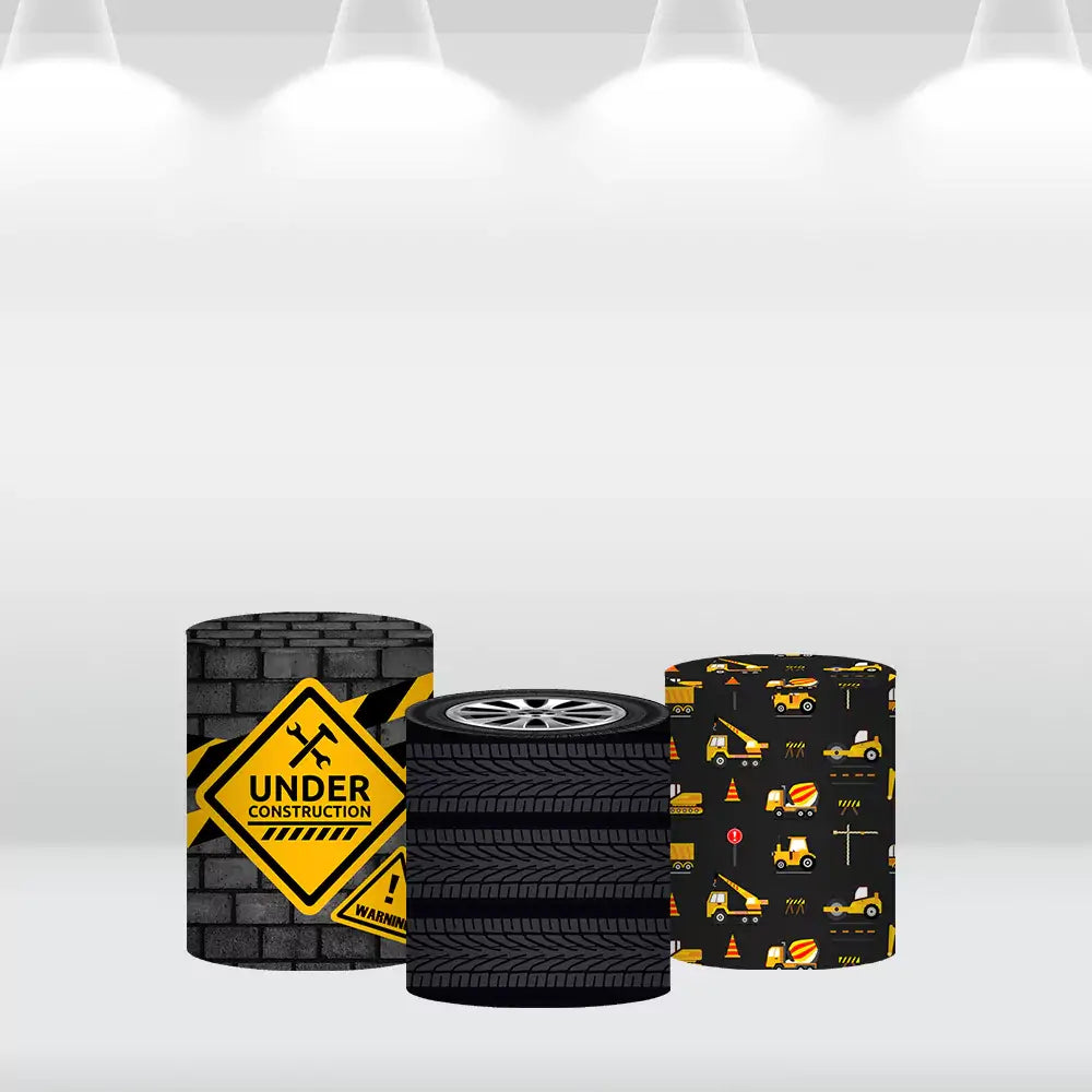 Set of three construction-themed cylinder covers featuring a caution sign with brick design, a tire stack pattern, and construction vehicles with tools and cones, complementing the backdrop.