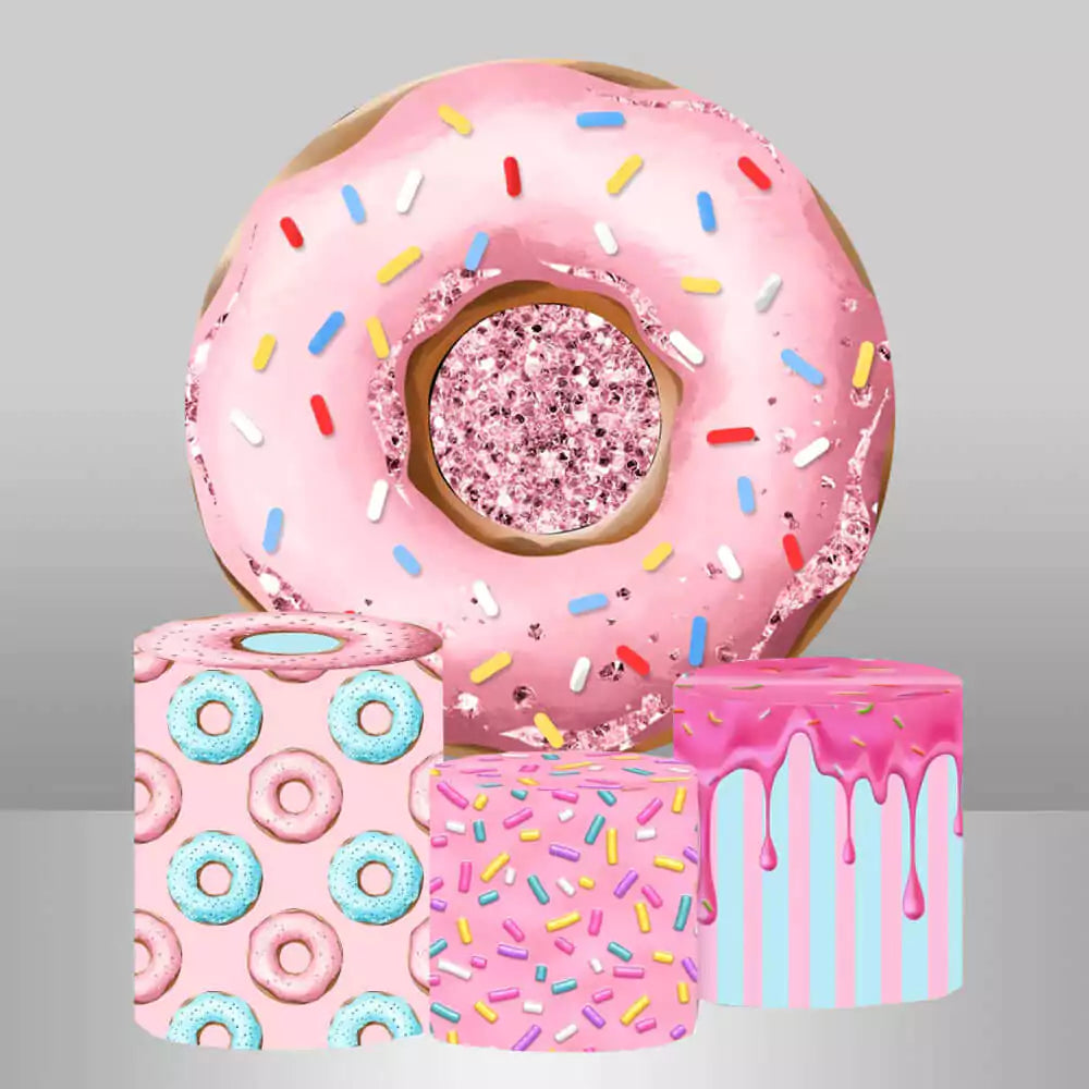 Donut-themed round backdrop featuring a large pink donut with sprinkles and matching cylindrical pedestal covers decorated with donut patterns, sprinkles, and icing designs.