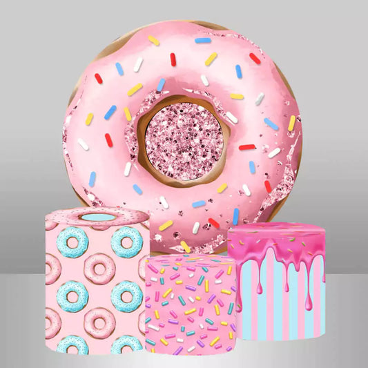 Donut-themed round backdrop featuring a large pink donut with sprinkles and matching cylindrical pedestal covers decorated with donut patterns, sprinkles, and icing designs.