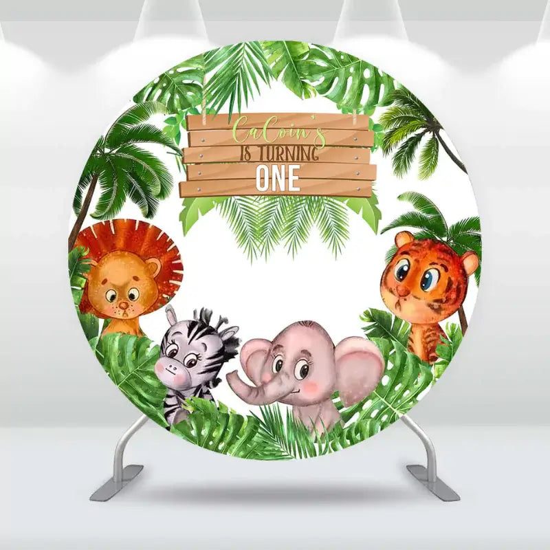 Jungle animal first birthday backdrop for Cucoin featuring a lion, zebra, tiger, and elephant surrounded by green palm leaves and the word 'ONE'.