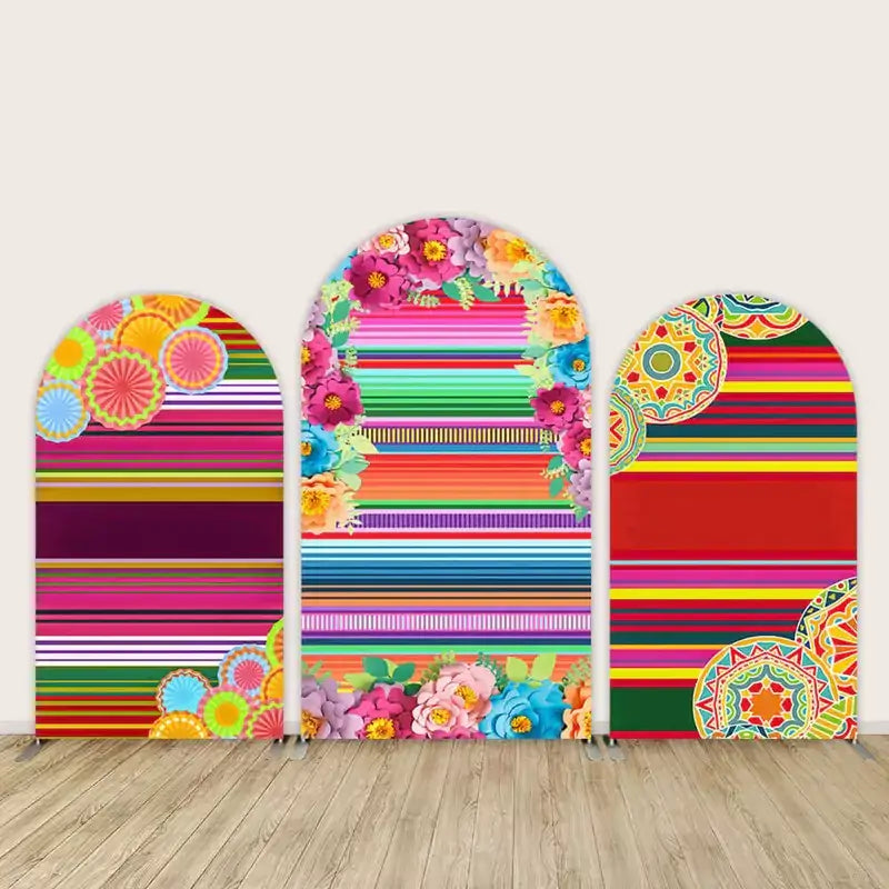 Three-panel arch backdrop set with colorful horizontal serape stripes, bright flowers, paper fan designs, and festive Mexican-style details.