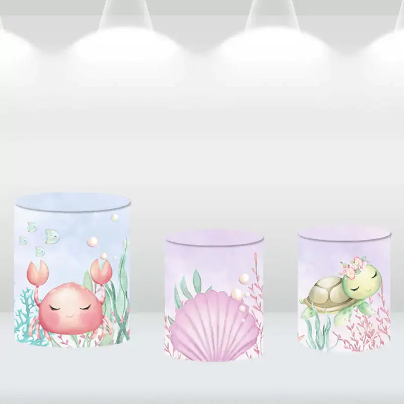Three matching cylindrical covers with underwater designs featuring a crab, turtle, and seashell, perfect for a sea-themed party.