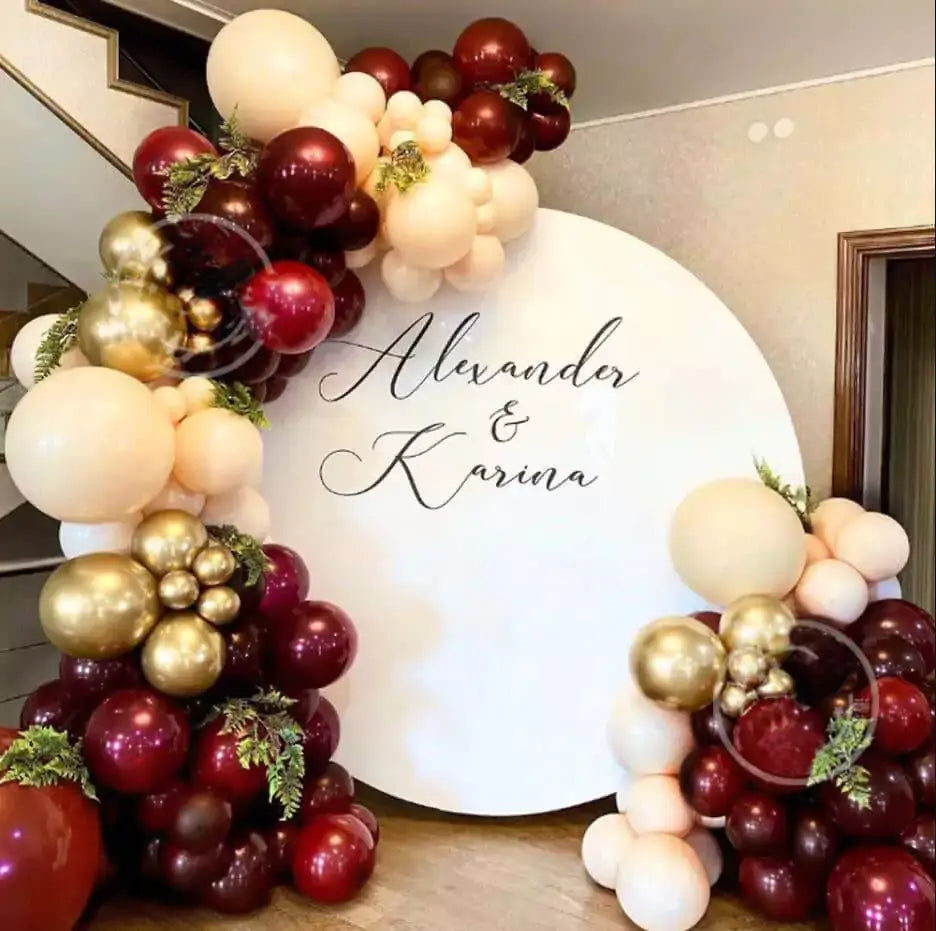 Elegant round wedding backdrop with personalized names ‘Alexander & Karina’ in script, decorated with burgundy, blush, and gold balloon garland