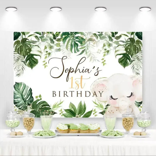 Tropical jungle-themed 1st birthday backdrop with watercolor leaves, gold accents, and a cute baby elephant – personalized for Sophia’s first birthday celebration.