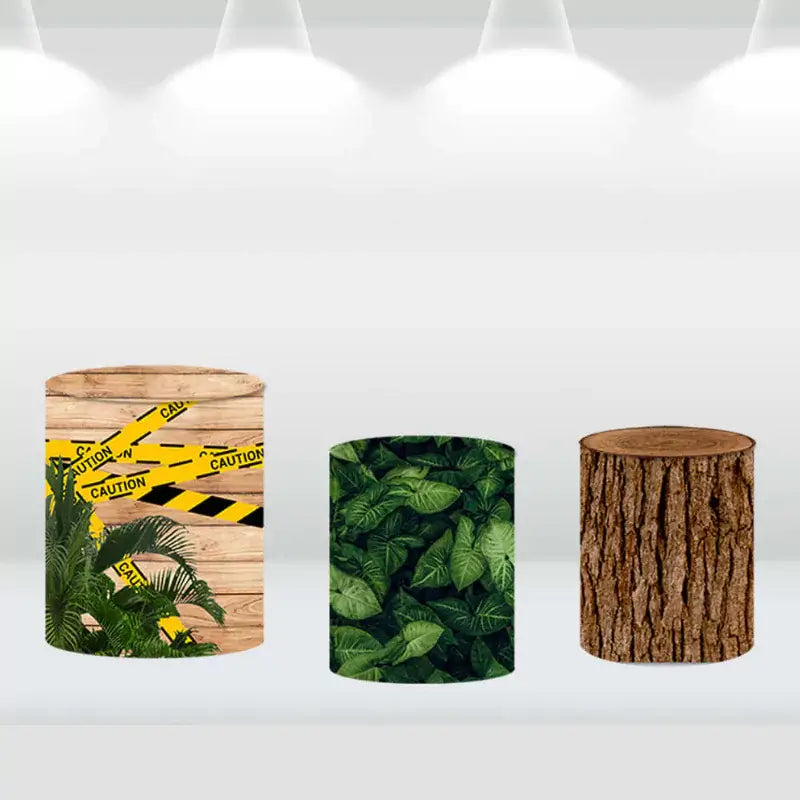 Cylinder covers designed with caution tape, jungle leaves, and a tree trunk pattern, matching the dinosaur-themed party backdrop.