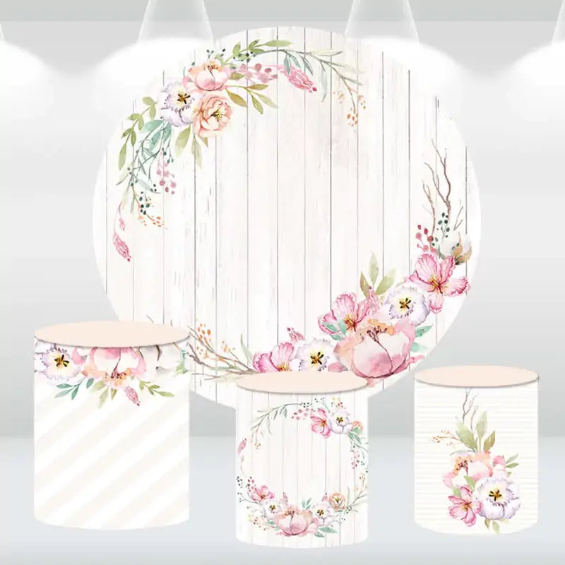 Floral-themed party decor set with a round backdrop featuring a watercolor flower wreath on a rustic wood background, along with matching cylinder covers.