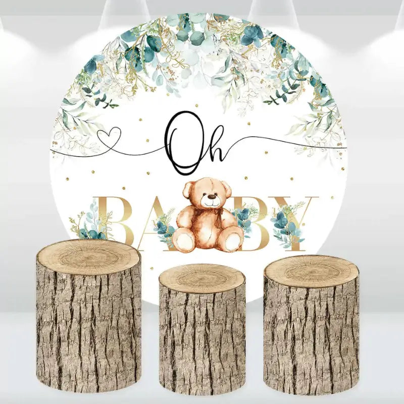 Rustic baby shower decor set with a teddy bear and greenery backdrop, complemented by log-style cylinder covers