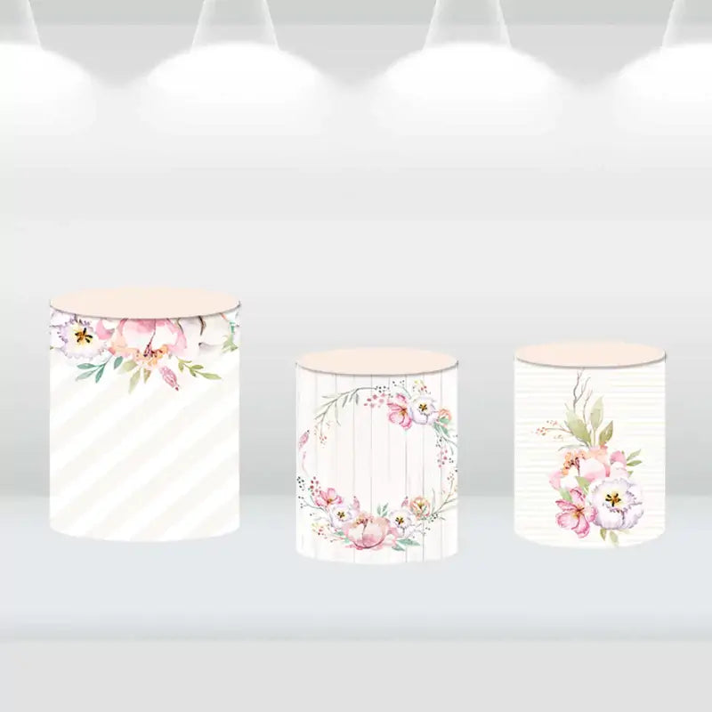 Floral-themed cylinder covers with watercolor flower patterns and rustic wood accents, complementing the party backdrop.