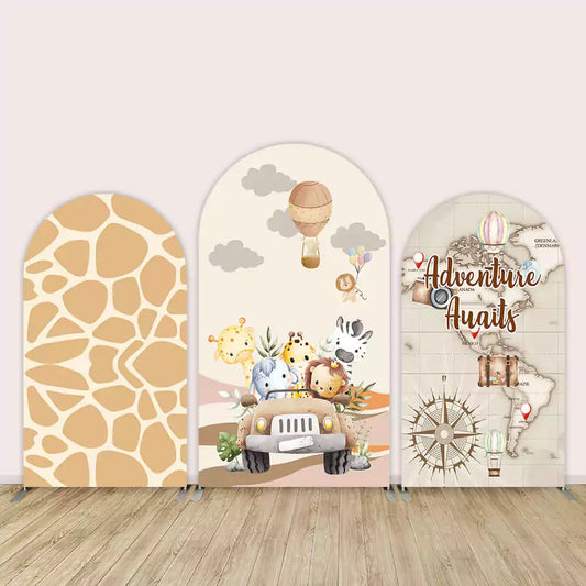 Three-panel arch backdrop with giraffe print, baby safari animals in a jeep under hot air balloons, and a world map with “Adventure Awaits” text.