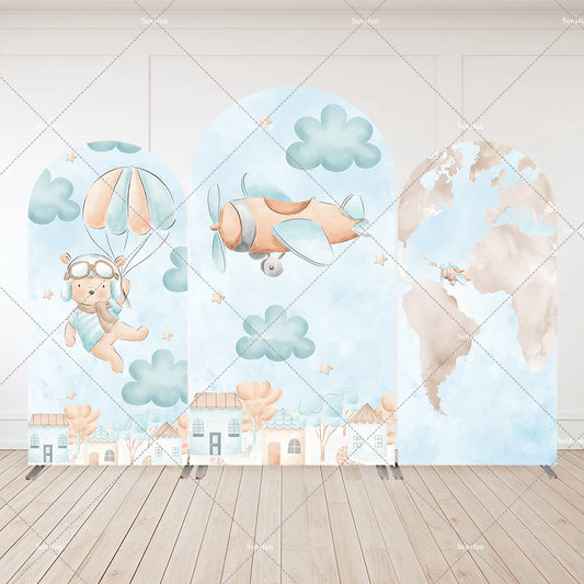 Three-panel aviator-themed arch backdrop featuring a teddy bear with parachute, flying airplane, world map, clouds, and pastel village scene.