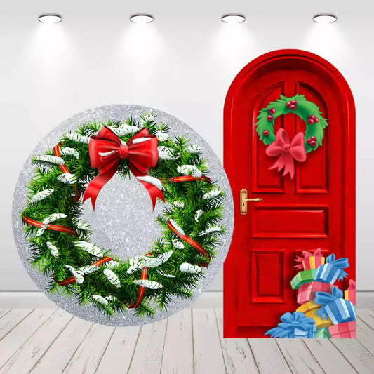 Christmas-themed backdrop set featuring a snowy wreath with a red bow and a red door decorated with a holiday wreath and stacked gifts, perfect for festive holiday events.