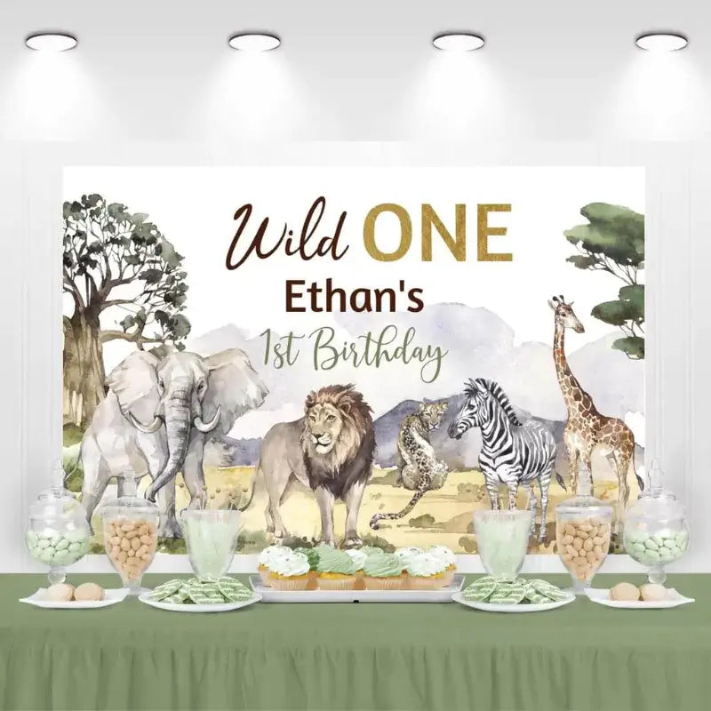 Safari birthday party backdrop with 'Wild One Ethan's 1st Birthday' surrounded by elephant, lion, and giraffe illustrations.