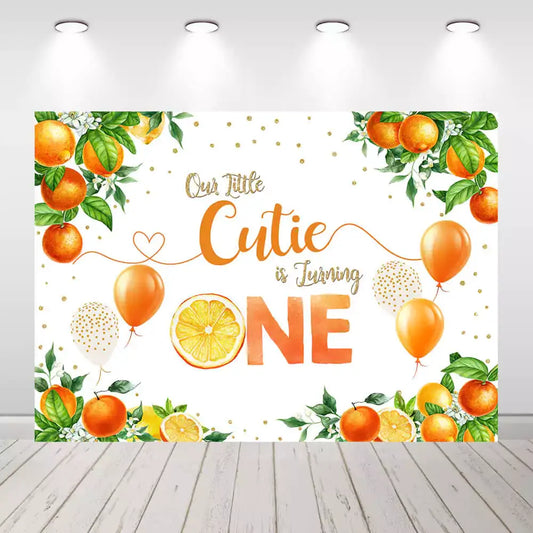 Orange-themed first birthday backdrop with "Our Little Cutie is Turning One" text and citrus designs, perfect for 1st birthday celebrations.