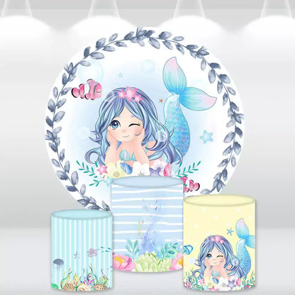 Mermaid-themed party backdrop with a cute winking mermaid surrounded by underwater creatures, paired with three matching cylindrical pedestal covers decorated with ocean and mermaid designs.