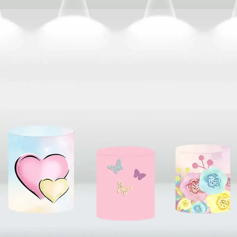 Set of three cylindrical pedestal covers with designs featuring hearts, butterflies, and pastel flowers, perfect for event décor.