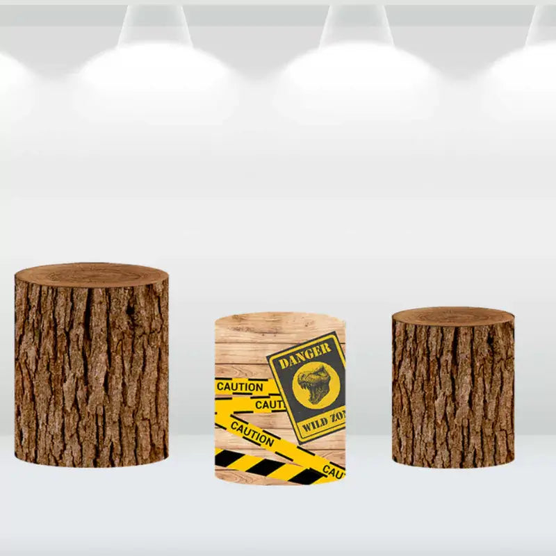 Three matching cylindrical covers with rustic tree log designs and a 'Danger: Wild Zone' caution tape pattern, ideal for a dinosaur-themed party backdrop.