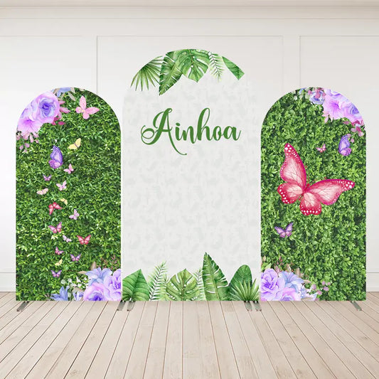 Three-panel personalized butterfly garden arch backdrop with hedge greenery, tropical leaves, purple and pink butterflies, and the name “Ainhoa.”
