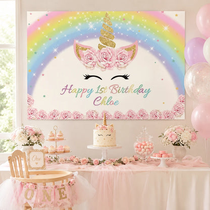 Rainbow unicorn first birthday backdrop with gold horn, pink roses, pastel stars and personalized name for a girls birthday party.
