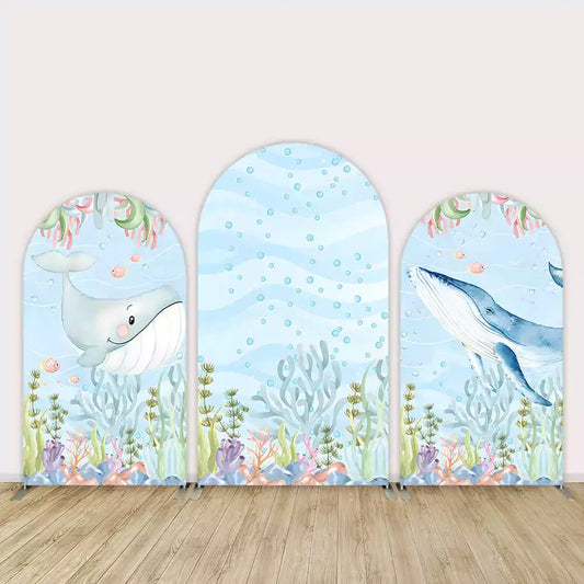 Three-panel arch backdrop with underwater scene including cartoon whales, seaweed, coral, fish, and soft watercolor bubbles on a blue ocean background.