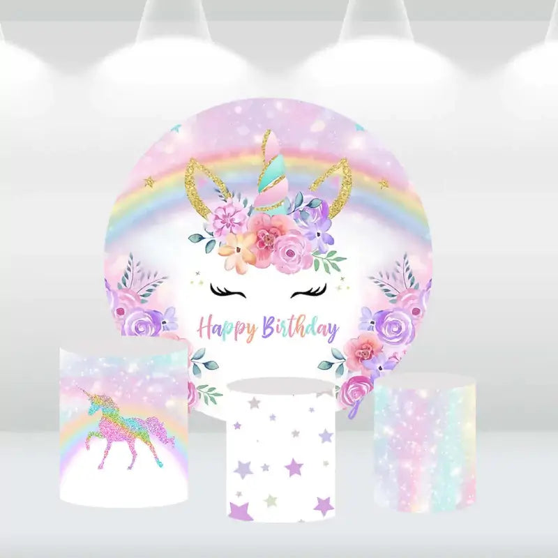 Unicorn-themed round birthday backdrop featuring a pastel rainbow, floral unicorn horn, and matching cylindrical pedestal covers with glittery unicorn, stars, and pastel designs.