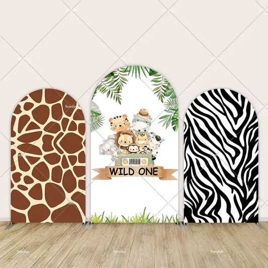 Three-panel safari-themed arch backdrop with giraffe print, “Wild One” sign and baby animals in jeep, and zebra print panel. 