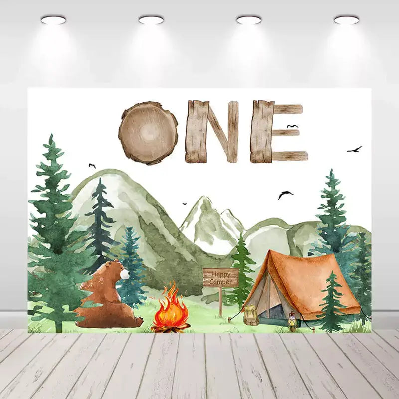 Camping-themed first birthday backdrop with tent, trees, and mountains.